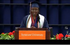 Woman with glasses and commencement regalia at orange and white Syracuse University podium