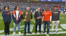 Alumni and John Wildhack holding football on football field