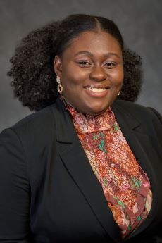 Woman smiling hair part in middle. Floral shirt and black jacket.