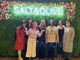 Three students are posed with four professors under a lit sign that reads "Salt and Olive."
