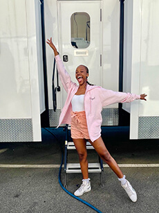Alumna in pink jacket - arms extended in front of trailer door