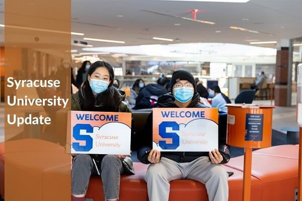 two students sitting with syracuse university welcome banner