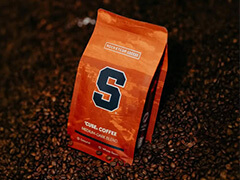 Orange bag of coffee with Syracuse logo in a pile of coffee beans
