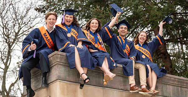 Class of 2024 graduates celebrate on campus by posing for a photo nearby the Hall of Languages.