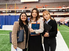 Three students stand together and smile at a career fair.